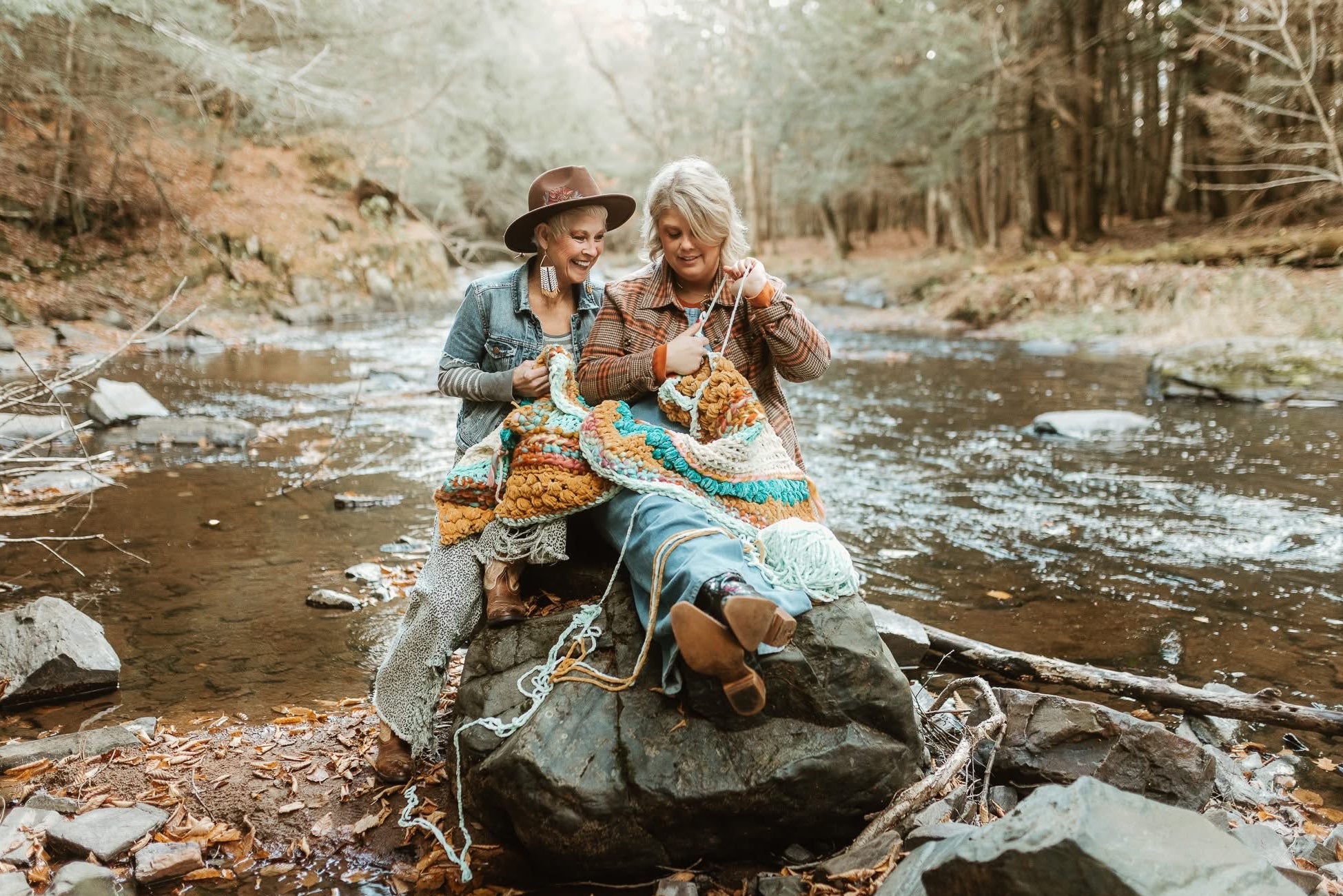 Two people sitting on a rock by a stream, surrounded by nature.